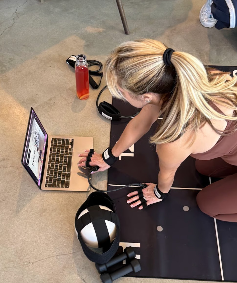 Woman using laptop during workout with fitness equipment nearby