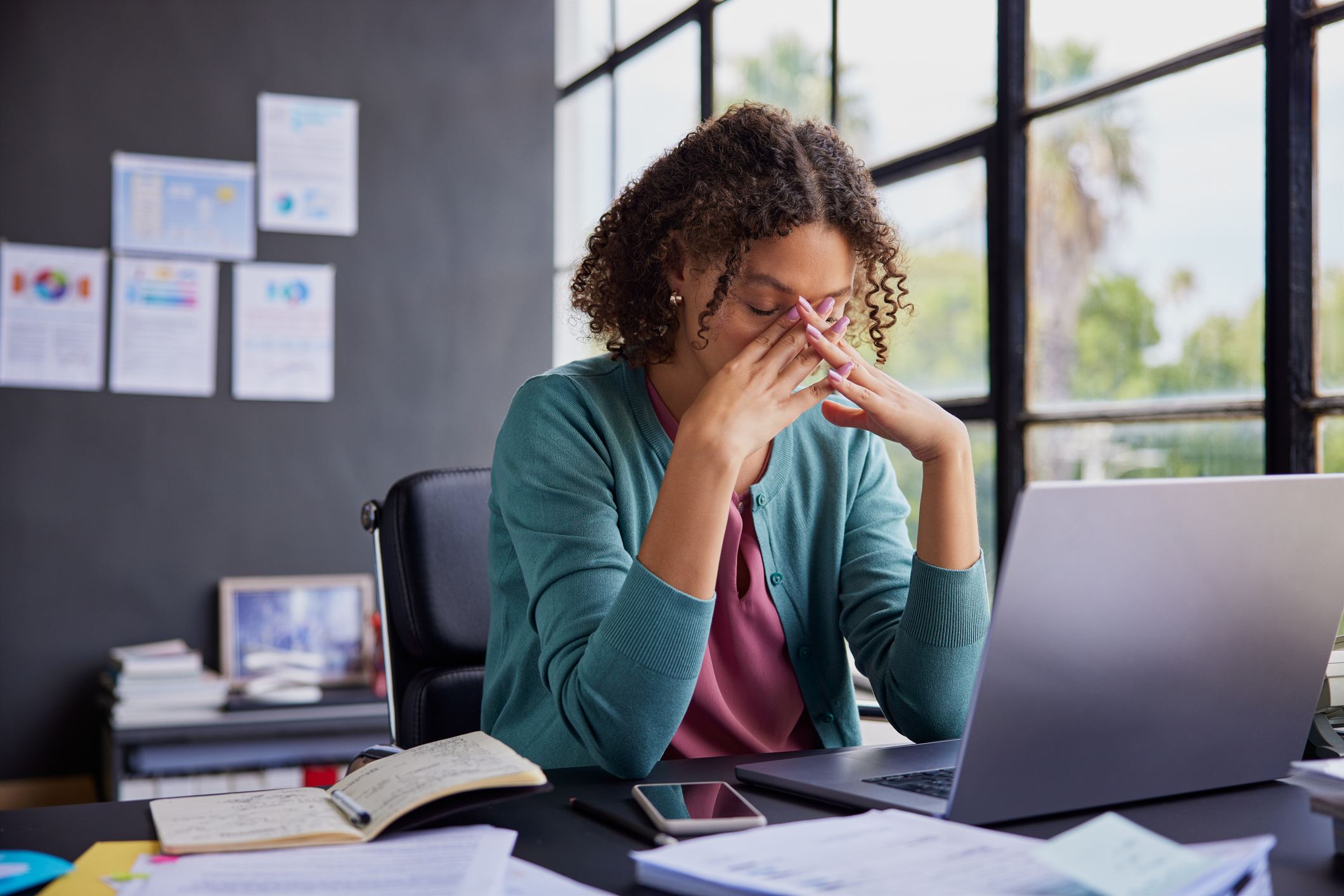 Woman sitting at a desk with her hands on her face, looking fatigued, one of the symptoms women should never ignore