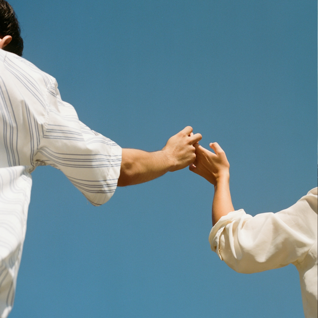 Two people holding hands against a clear blue sky