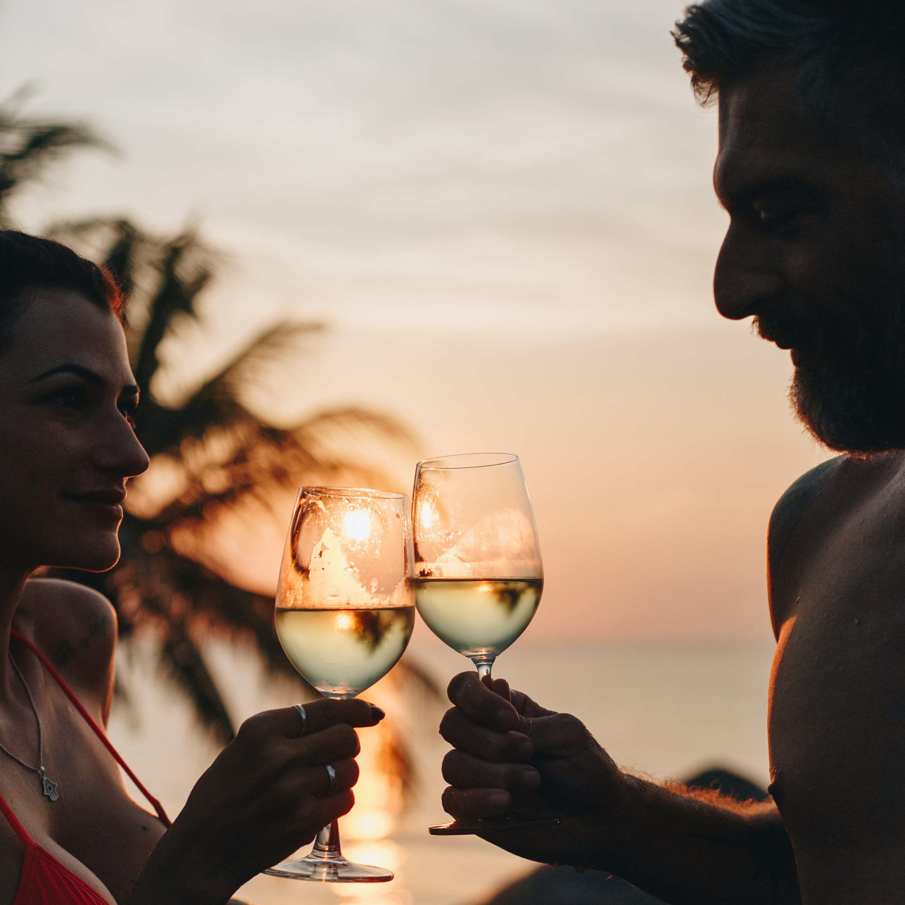 Couple toasting with wine glasses at sunset in a pool