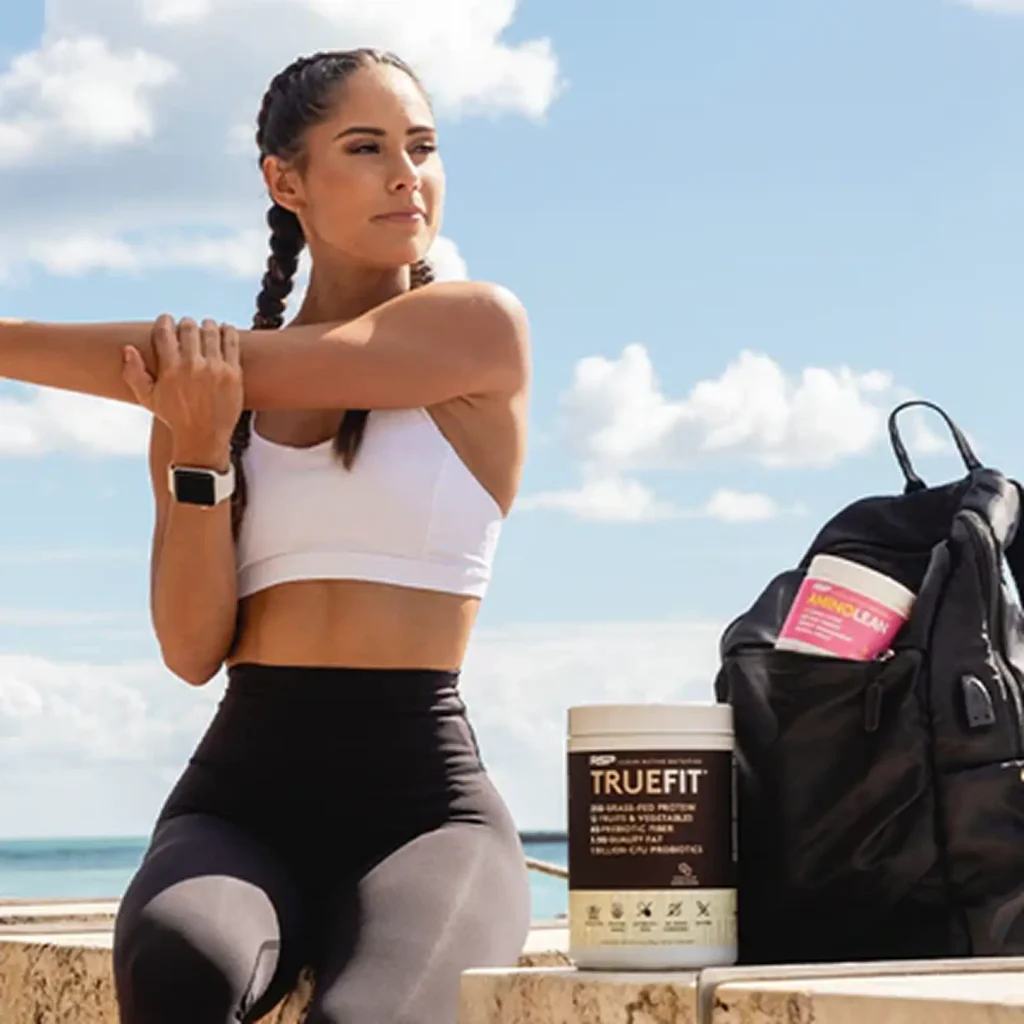 woman stretching her arms sitting on a wall with true fit next to her