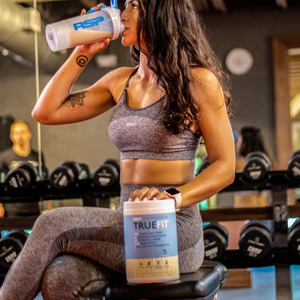 woman drinking truefit sitting on a gym bench